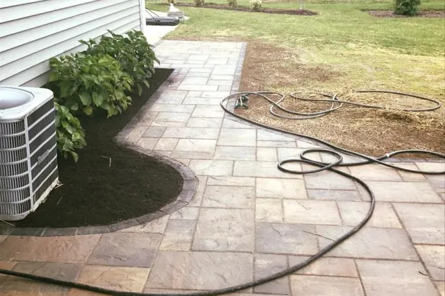 Large paver patio beside a house with a mulched border.
