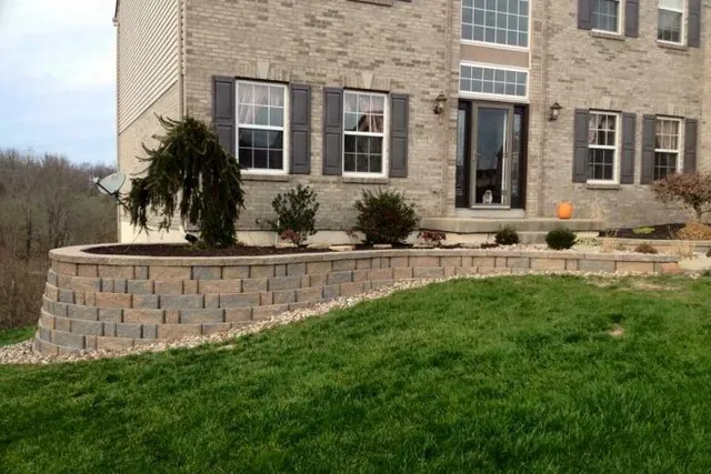 Block retaining wall curving along a sloped front lawn.